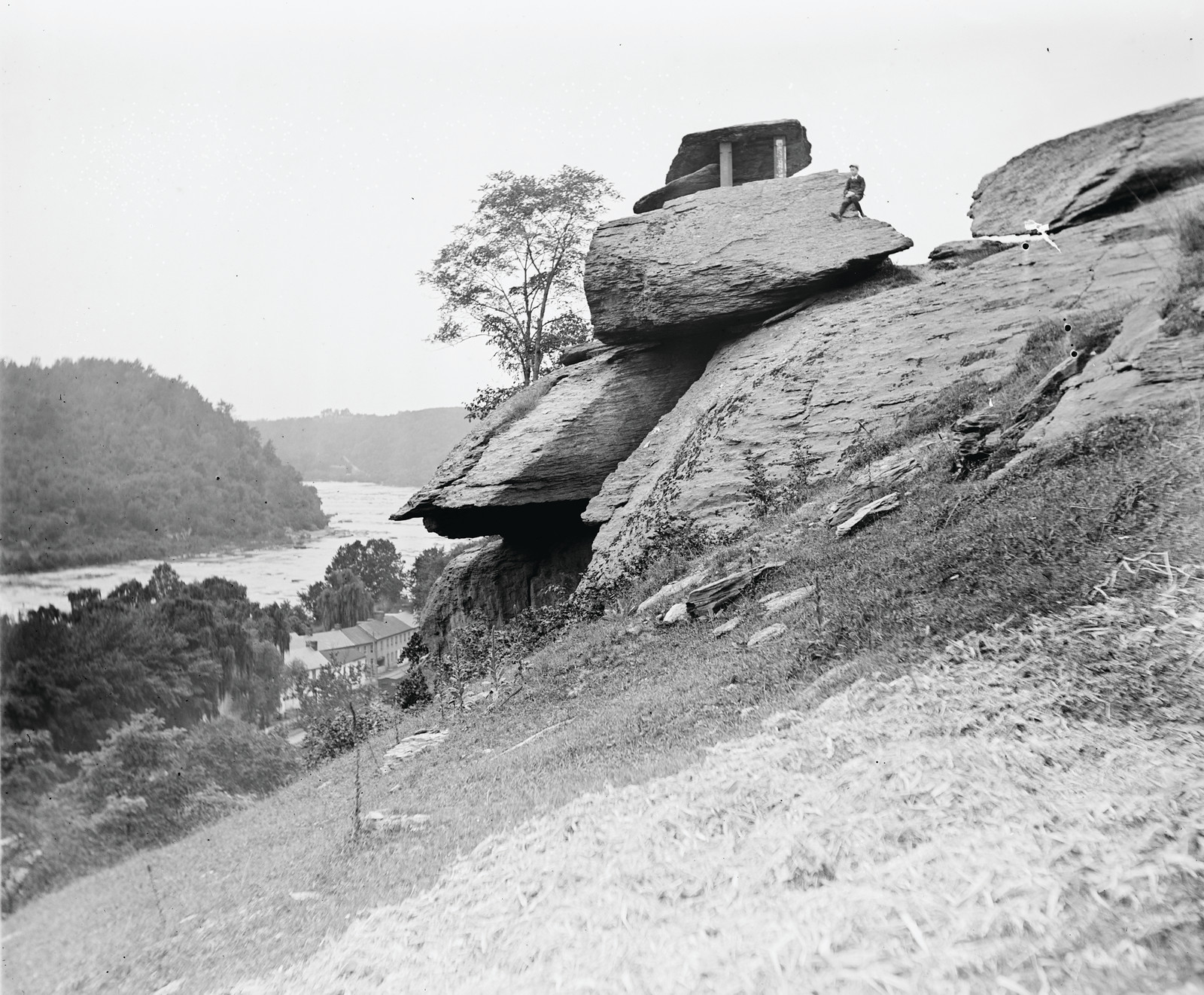 Rock outcrop above river with small shelter and man — historic image