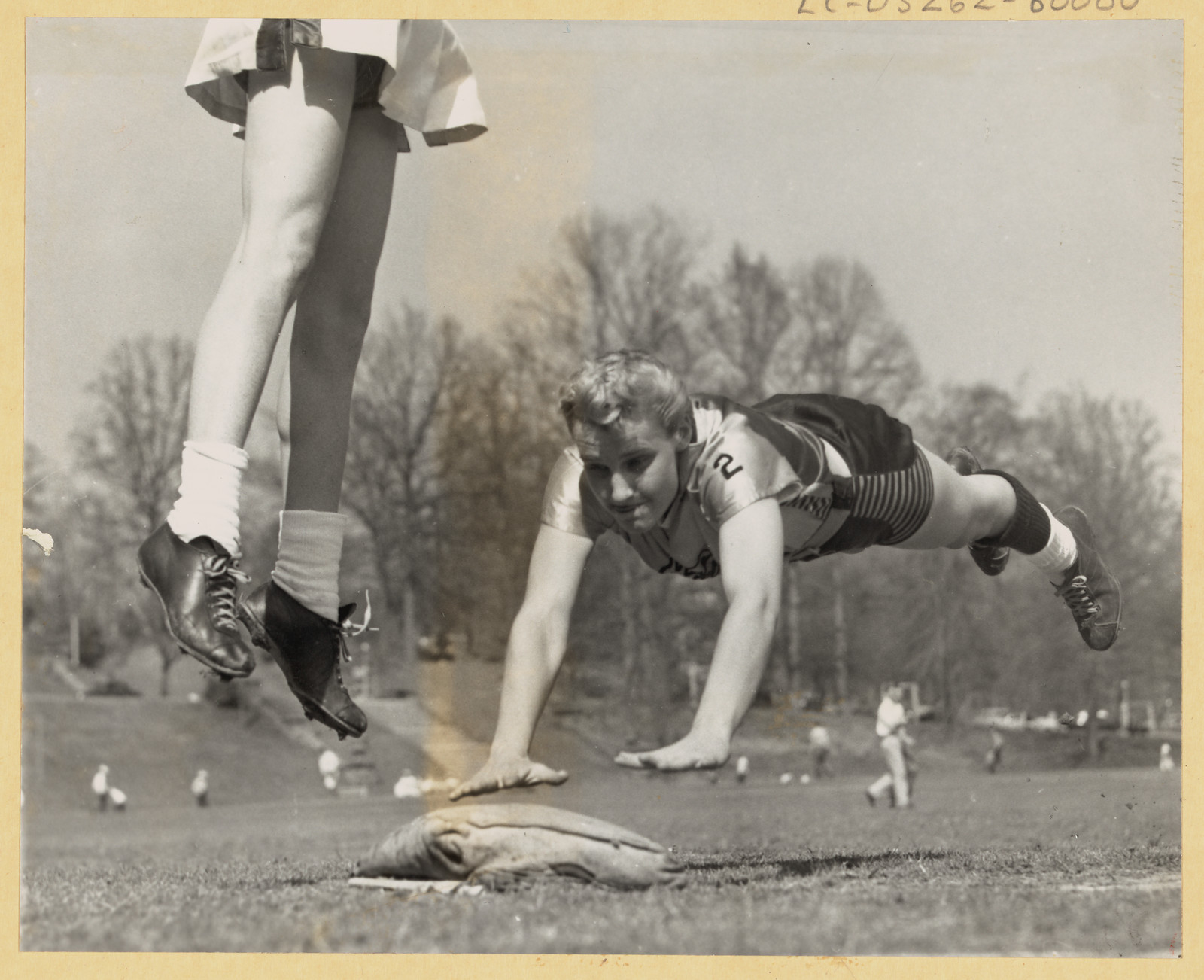 Women's baseball players sliding into base on a field — historic image