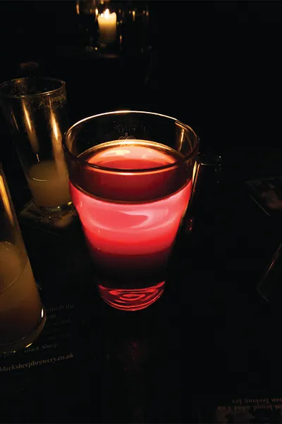Red-lit pint glass beside candle in a dark pub