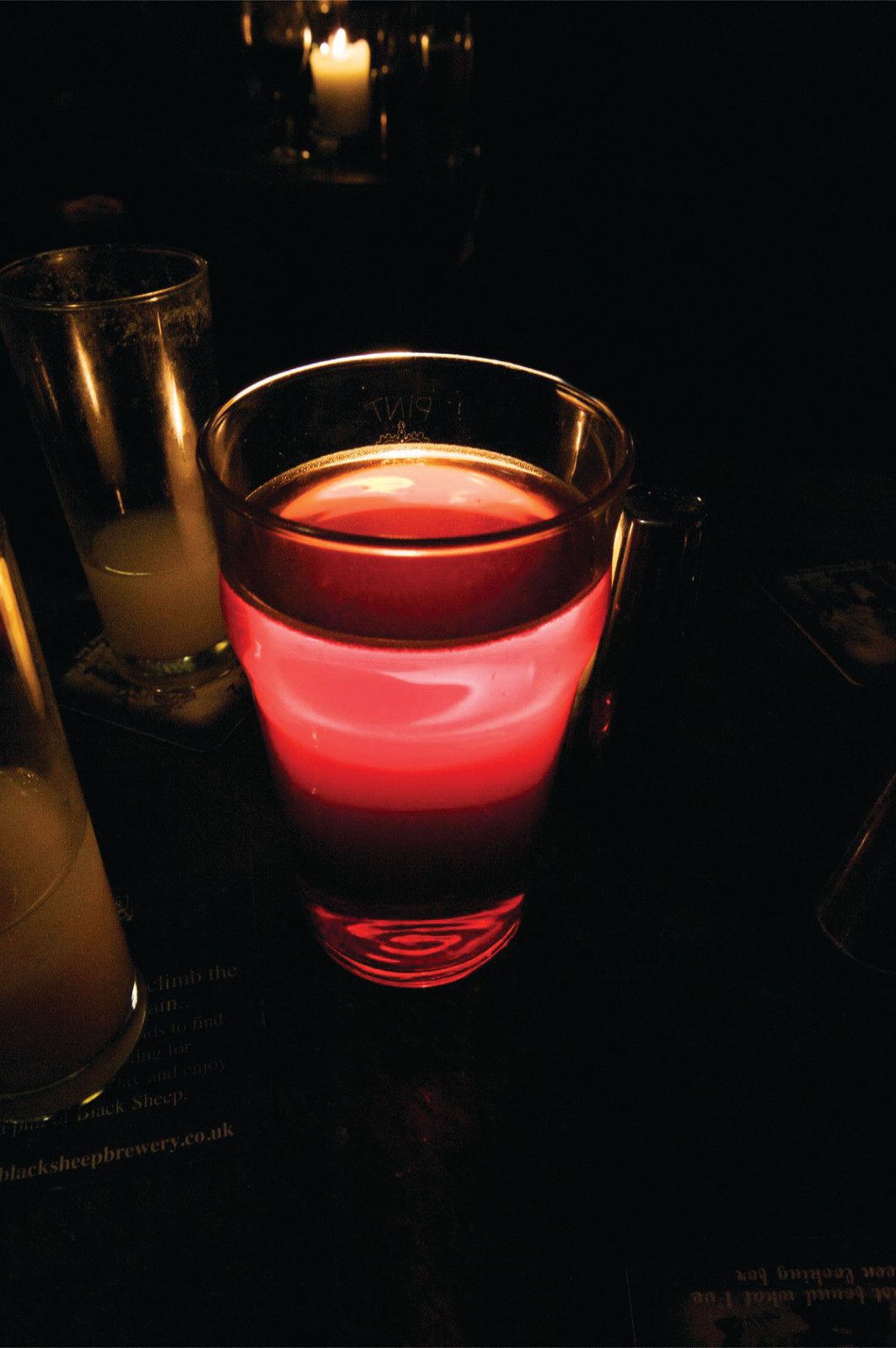 Red-lit pint glass beside candle in a dark pub — historic image