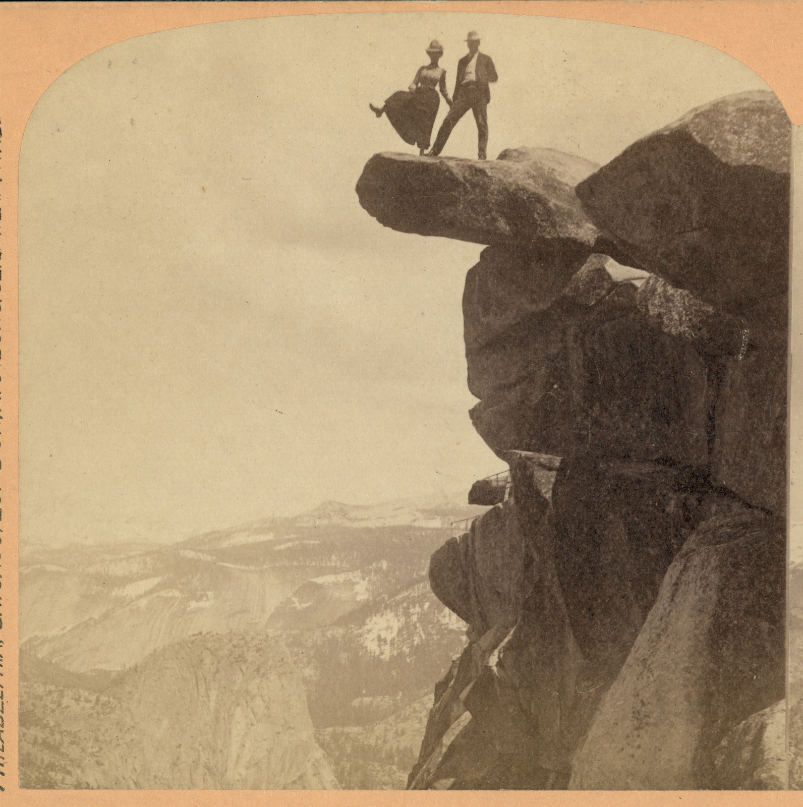 Two people standing on a rocky overhang above a mountain valley — historic image