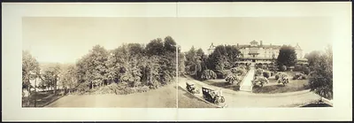 Panoramic sepia photograph of a large hotel with automobiles
