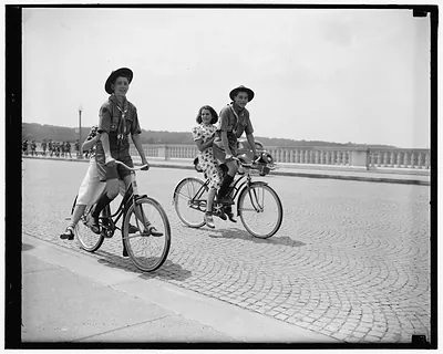 Two Scouts on bicycles with a girl on a cobbled road
