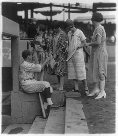 Bucky Harris autographing scorecards on dugout steps, on Ladies Day