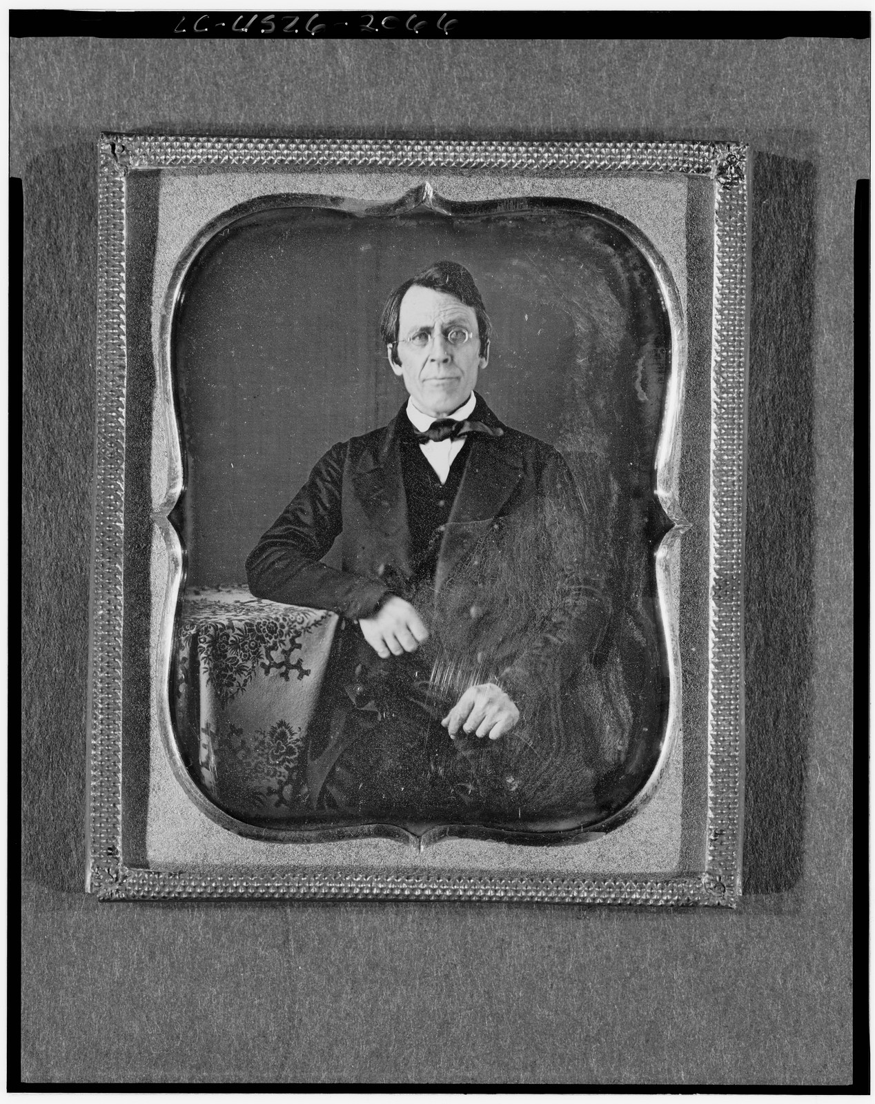 [Unidentified man wearing spectacles, half-length portrait, seated, facing front, arm on table with tablecloth], [between 1840 and 1860] — historic photograph