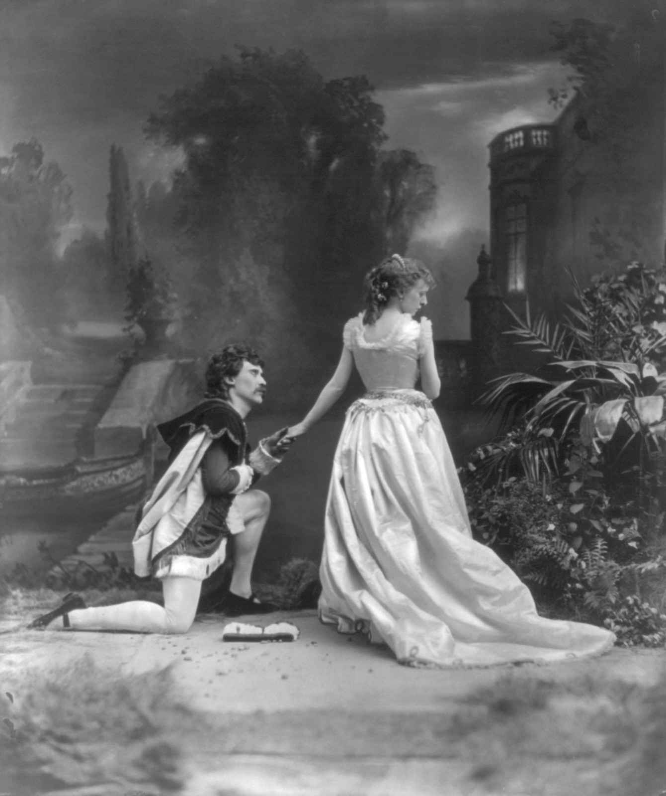 Man kneeling to a woman in a gown before a painted garden — historic image