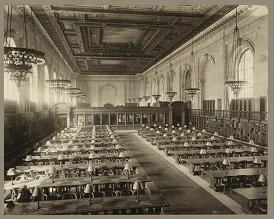 Large public library reading room with long tables and lamps