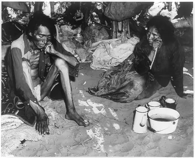 [Navajo man and woman sitting on floor in a hogan]