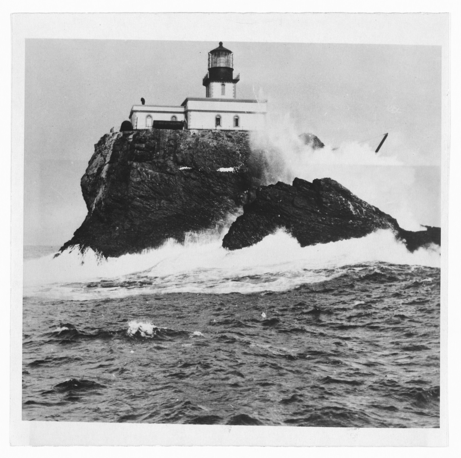 Lighthouse on a rocky islet in heavy surf — historic image