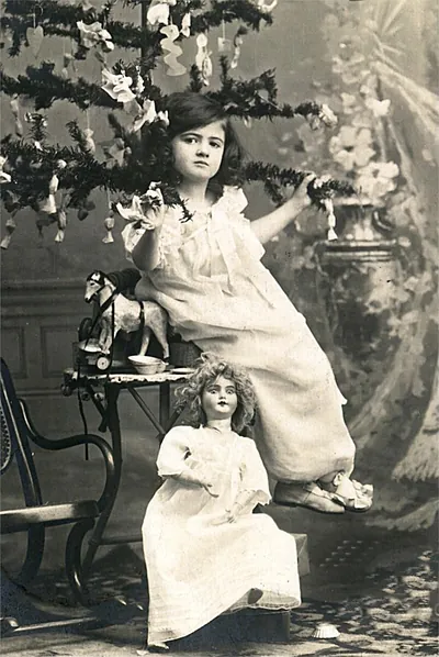 Girl in white dress beside Christmas tree and doll