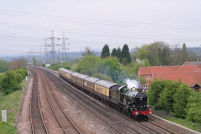 Steam locomotive hauling passenger coaches past a village