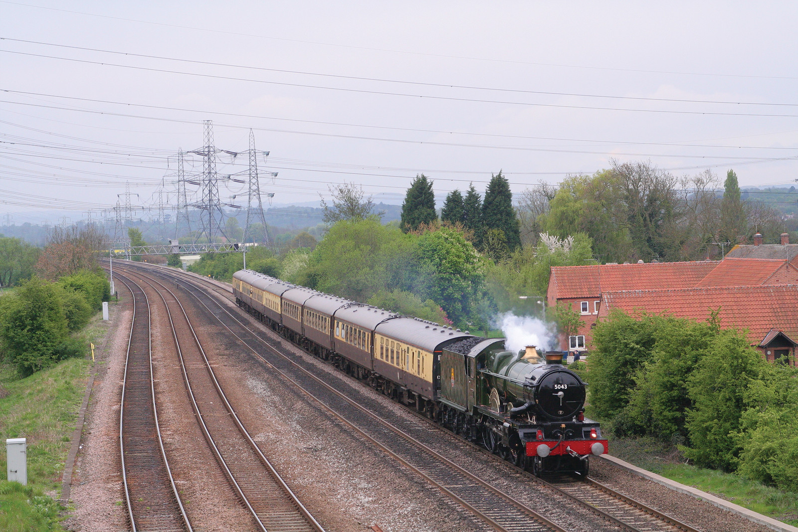 Steam locomotive hauling passenger coaches past a village — historic image