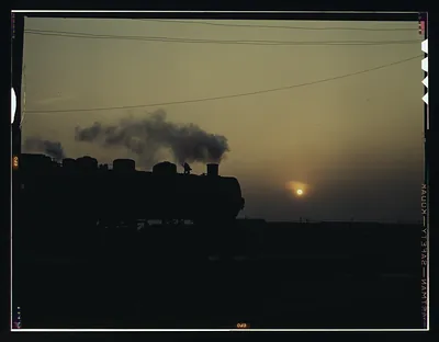 Steam locomotive silhouetted at sunset with smoke rising