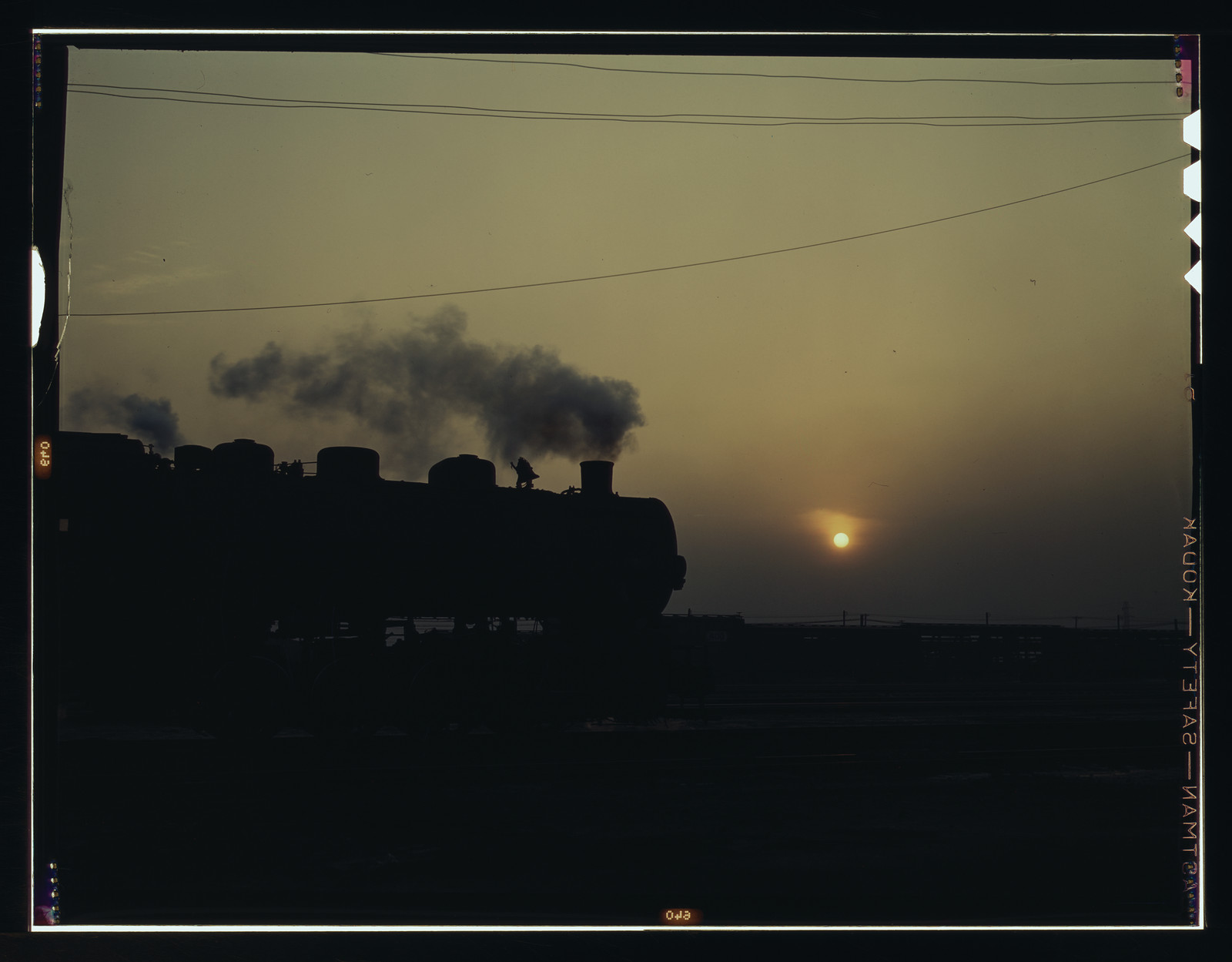 Steam locomotive silhouetted at sunset with smoke rising — historic image