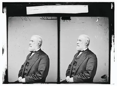 Bearded man in dark suit and bow tie, seated in profile