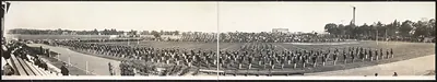 Panoramic photograph of massed marchers on an athletic field before crowded stands