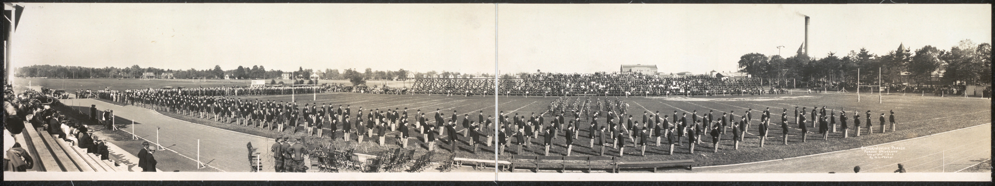 Panoramic photograph of massed marchers on an athletic field before crowded stands — historic photograph