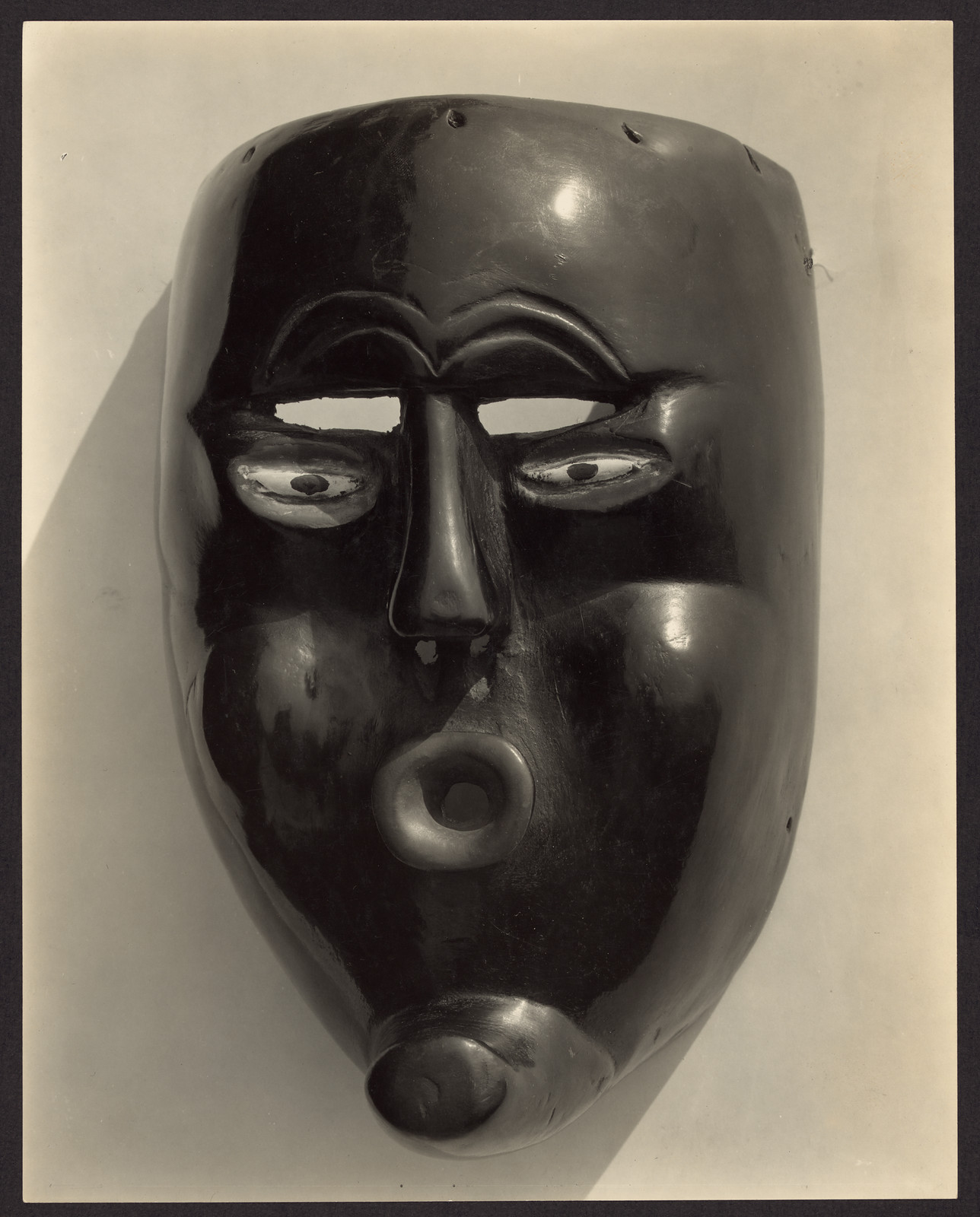 Glossy black mask with eye holes and protruding mouth — historic image