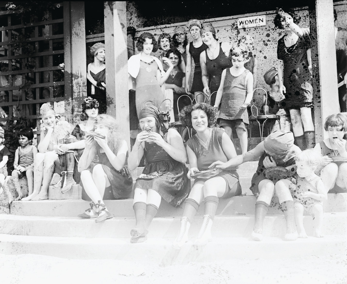 Women in bathing suits eating on beach steps — historic image