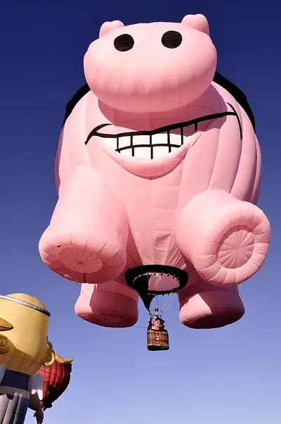 Large pink pig-shaped hot air balloon in blue sky
