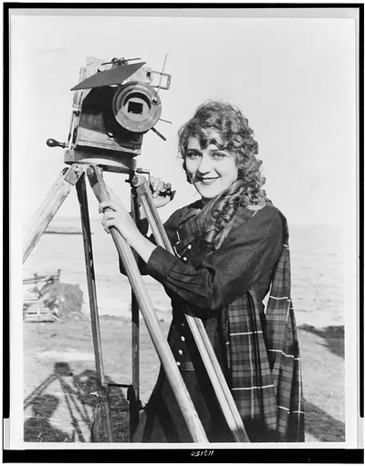 [Mary Pickford, half-length portrait, standing, facing slightly left, with motion picture camera, on beach]