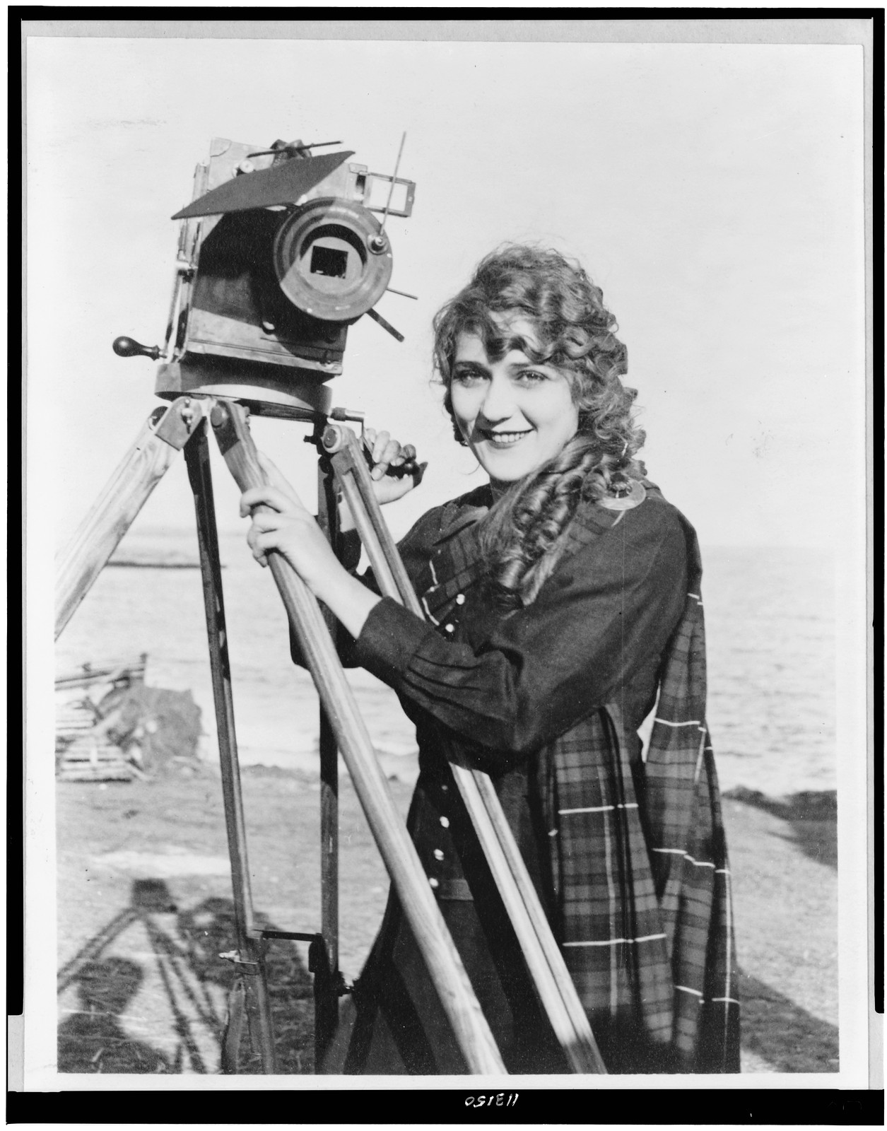 [Mary Pickford, half-length portrait, standing, facing slightly left, with motion picture camera, on beach], c1916. — historic photograph
