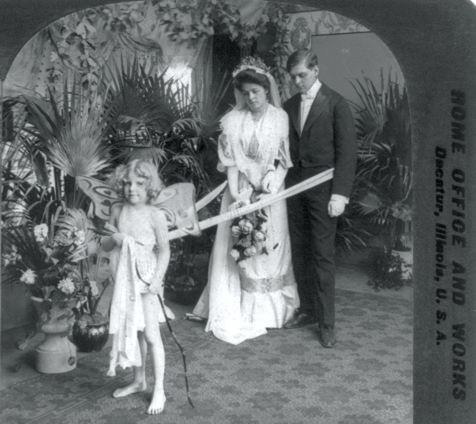 Bride and groom with Cupid in a staged studio setting — historic image