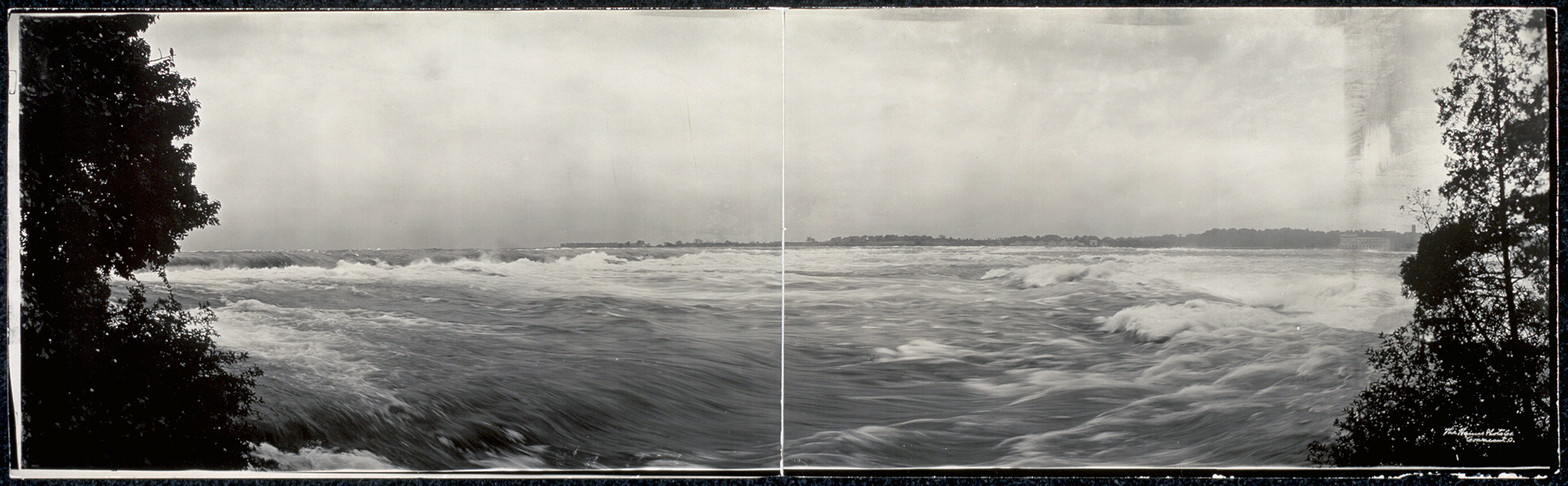 Panoramic black and white photograph of river rapids between trees — historic photograph