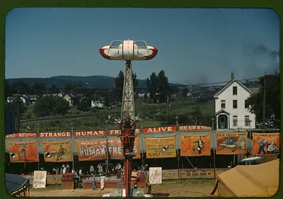 Fairground midway with sideshow banners and a tower ride