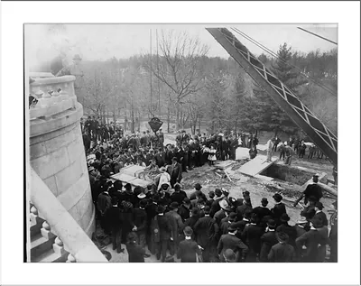 Large crowd watching a stone being lowered by derrick