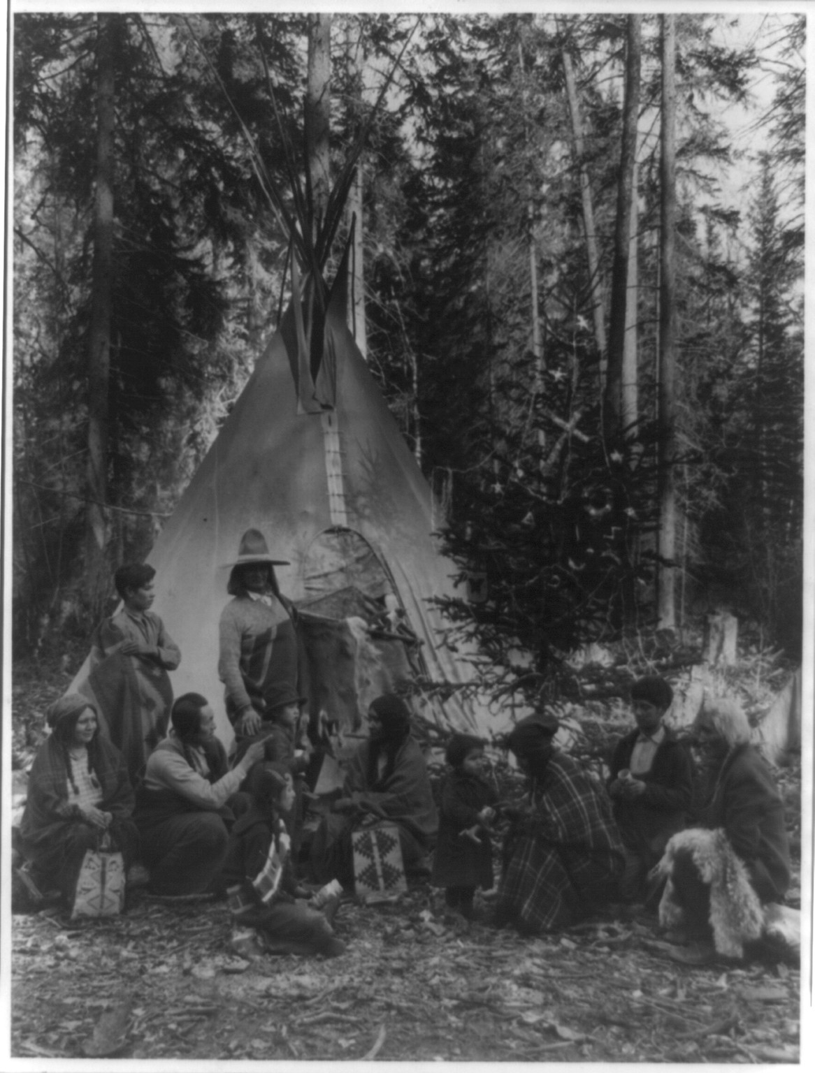 Flathead Indians holding pre-Christmas family gatherings on the west side of Glacier National Park, in the dense forest of evergreen trees that skirt the Rocky Mountains, [between 1900 and 1920(?)] — historic photograph