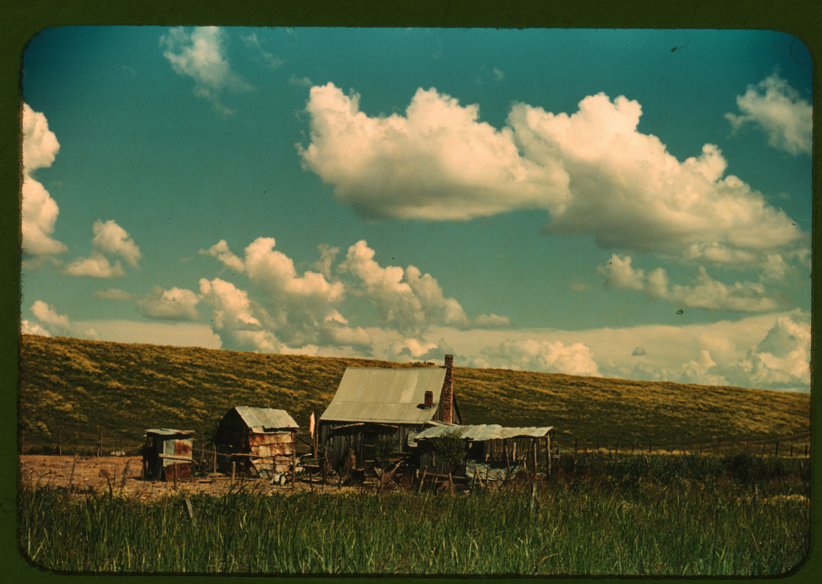 Small shacks and sheds on a grassy hillside under clouds — historic image