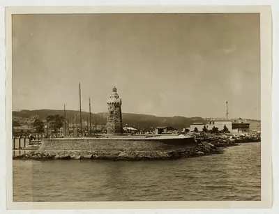 Stone lighthouse on a breakwater with sailboat masts