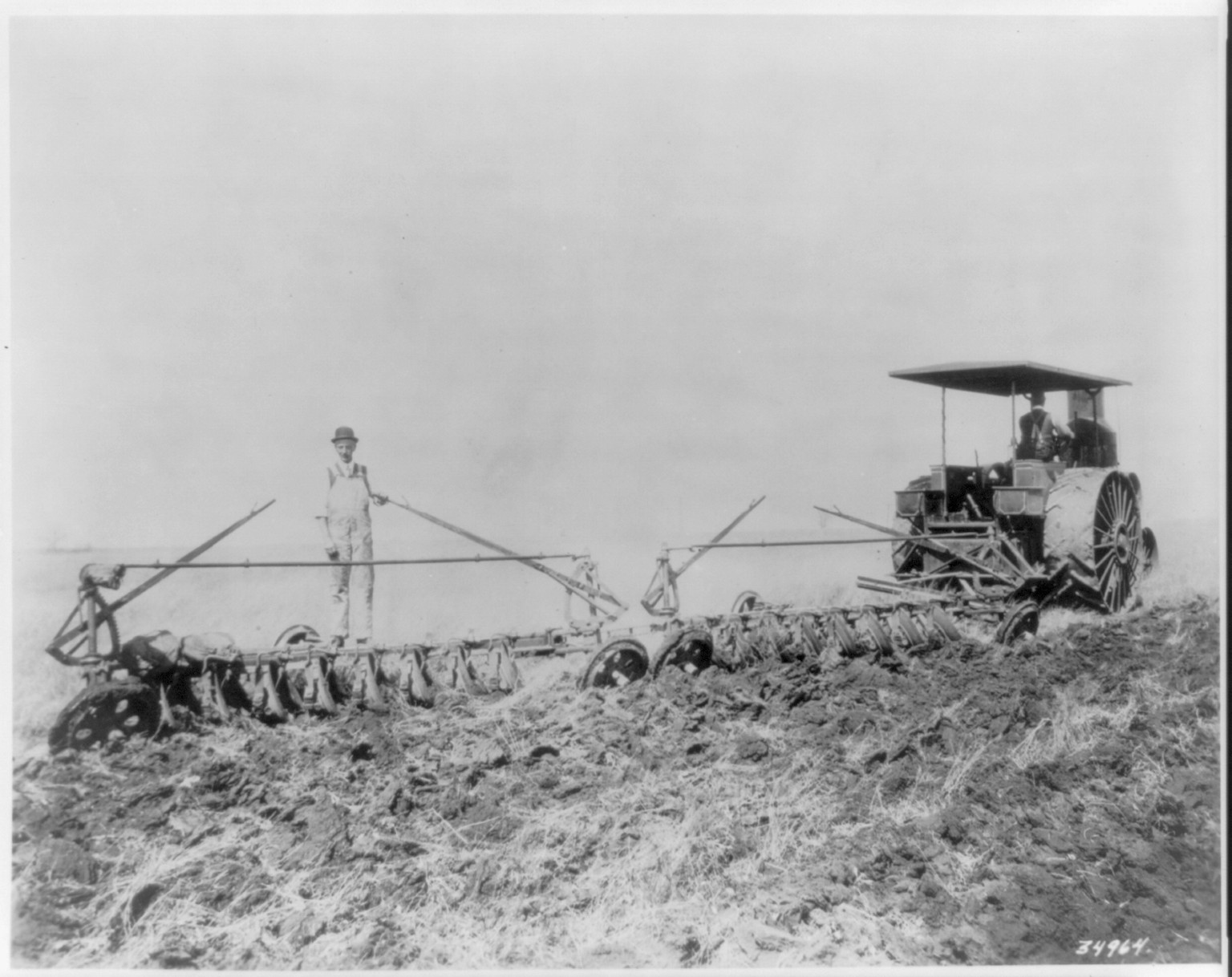[Tractor pulling large set of discs across field] — historic photograph