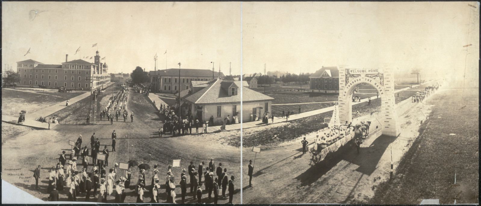 Panoramic photograph of parade passing a Welcome Home arch — historic photograph