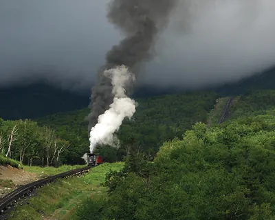 Steam locomotive pulling smoke up a forested mountain railway