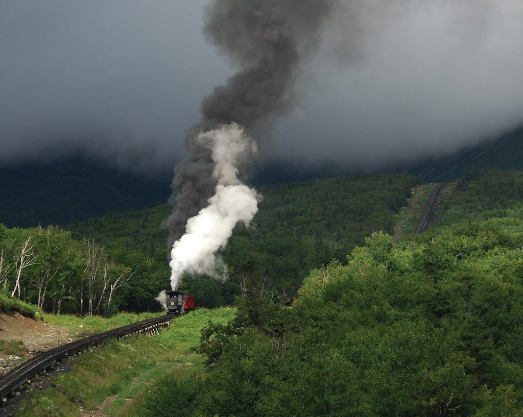 Steam locomotive pulling smoke up a forested mountain railway — historic image