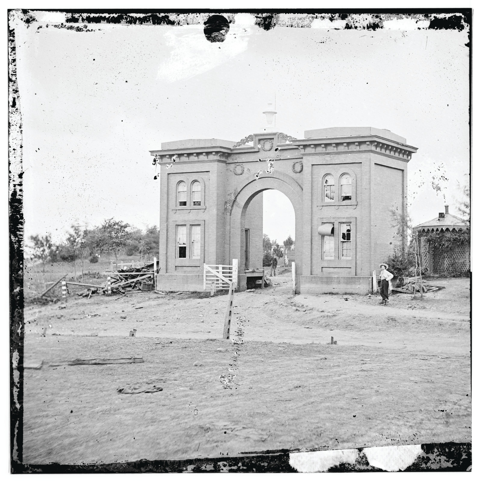 Brick arched cemetery gatehouse with a figure at right — historic image
