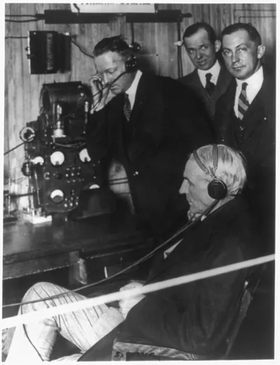 [Henry Ford, 1862-1947, three-quarters length portrait, seated, wearing radiophone receivers at Atlanta-Wonder, Atlanta, Ga, newspaper office, with 3 other men, left profile]