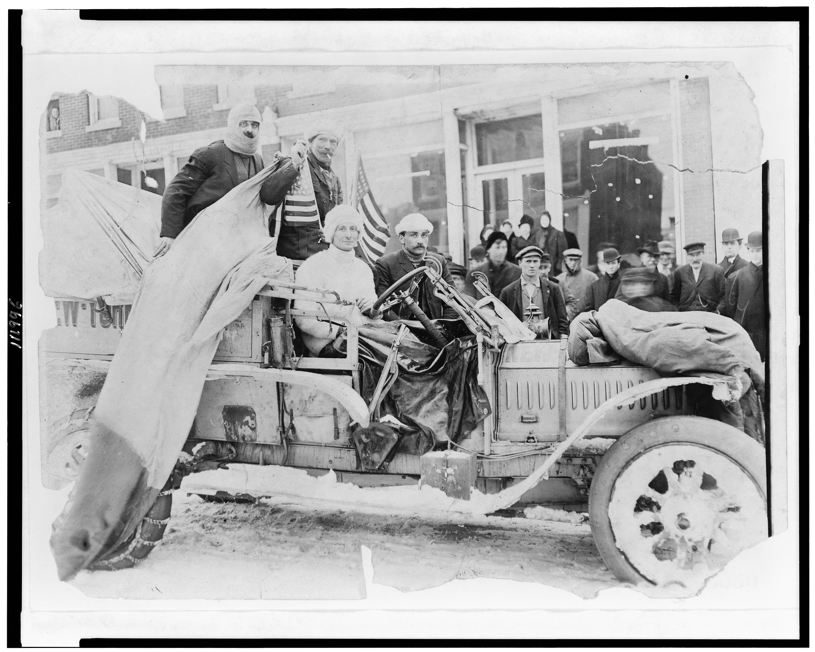 [Four men in automobile, with American flags on snow-covered street, on the New York to San Francisco leg of the 1908 New York to Paris automobile race], [1908] — historic photograph