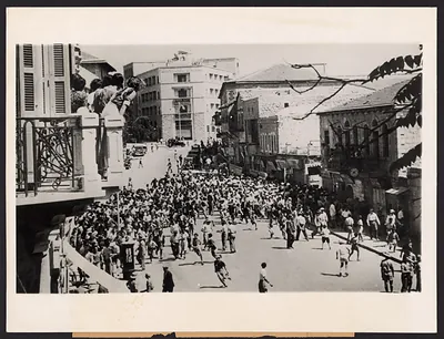 Crowd running through a city street, onlookers on balcony