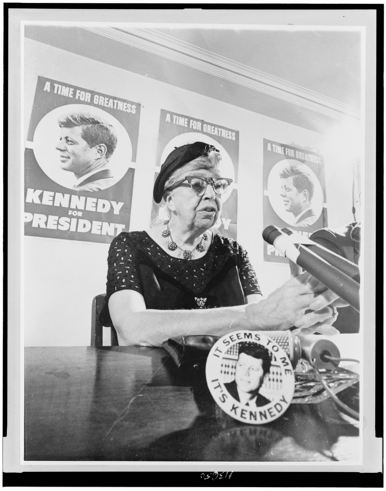 Woman speaking at microphone before Kennedy campaign posters — vintage poster