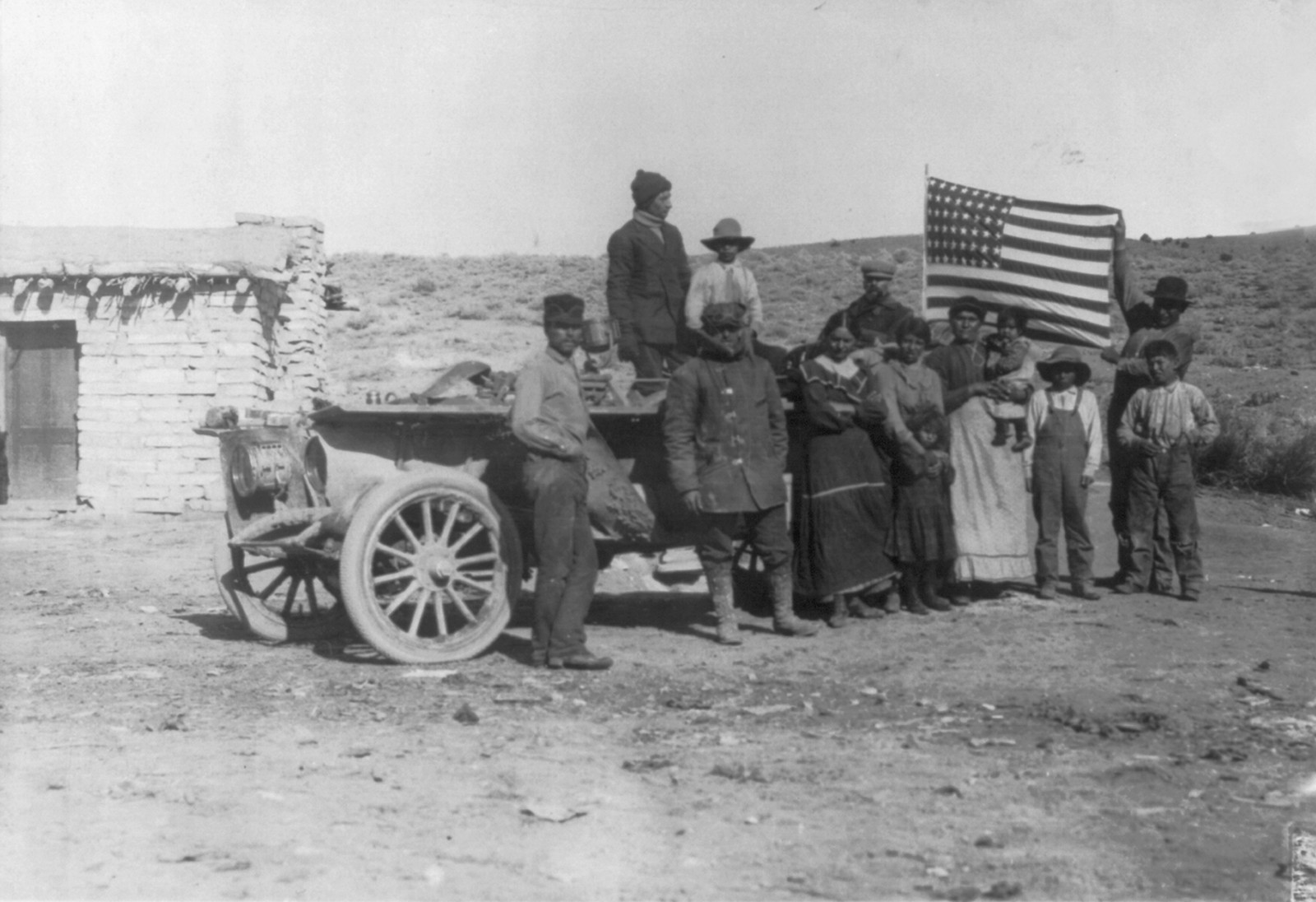 [New York to Paris auto race, 1908: drivers and Indians holding U.S. flag posed by auto in front of house], [1908] — historic photograph