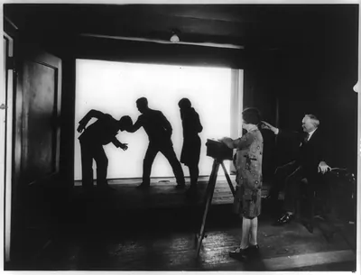 [Dr. C. Francis Jenkins, noted inventor and television pioneer, directing a scene in his new studio in Washington, D.C., the first devoted exclusively to the production of motion pictures to be shown to an audience by radio; note that the performers are shown in silhouette, that being the form in which the pictures are received over the air, and that the cameraman is a girl]