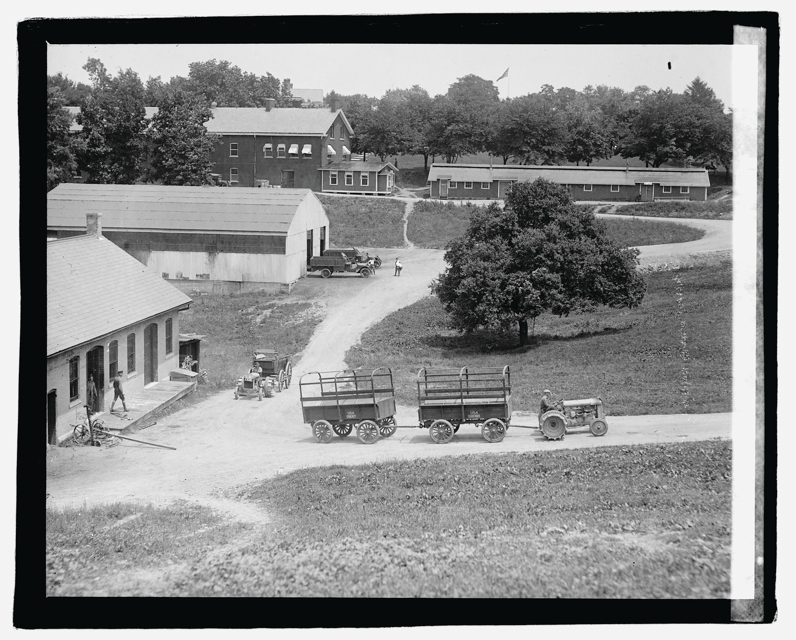 Tractor pulling two wagons on a farm road — historic image