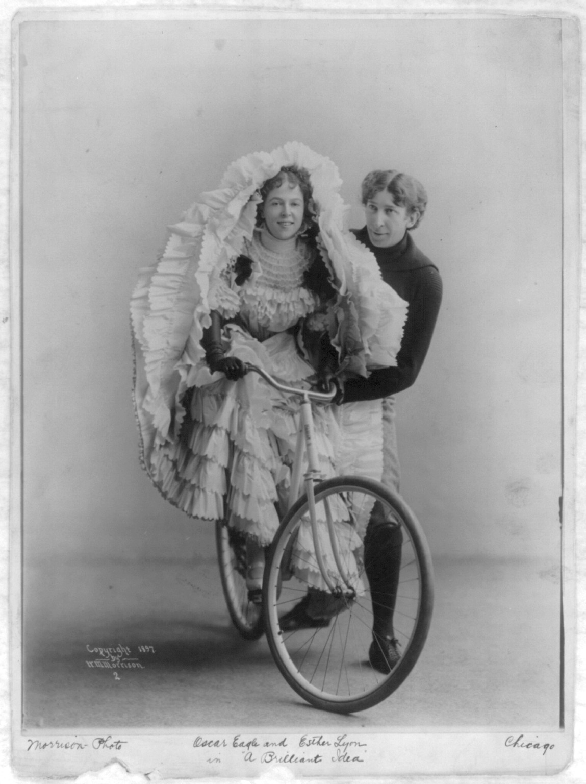 Oscar Eagle standing alongside of Esther Lyon (on bicycle), in A Briliant Idea"", c1897. — historic photograph