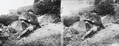 Bearded man with sketchbook seated on rocks, stereo photograph