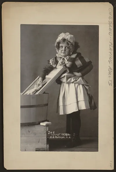 [Girl wearing eyeglasses, bonnet and apron, with washboard and tub]