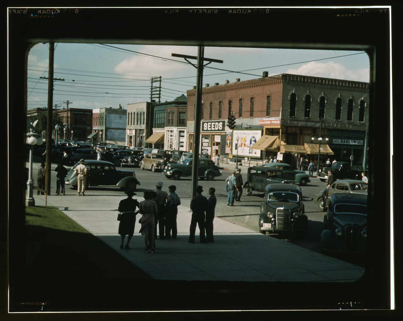 Downtown street corner with SEEDS sign and parked cars — historic image