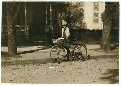 Boy with delivery bicycle and newspaper basket on street